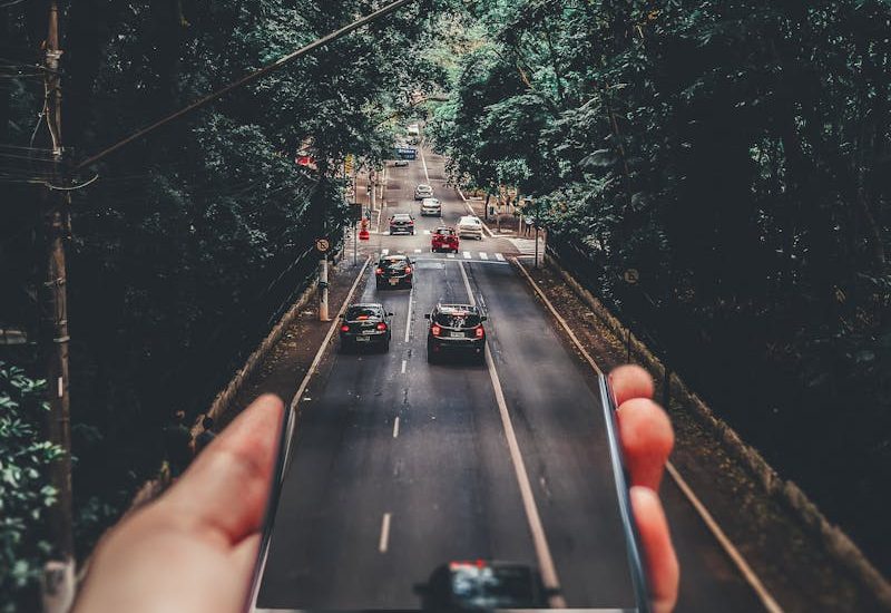 Forced Perspective Photography of Cars Running on Road Below Smartphone